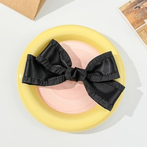Close-up of elegant black satin bow hair clip with layered ruffles and smooth silk texture