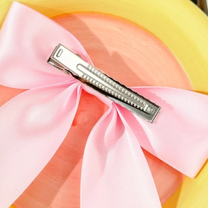 Detail of pink satin bow hair clip showing the durable silver metal alligator clip base