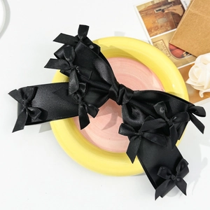 Elegant black satin oversized bow hair clip decorated with mini bows on a colorful plate