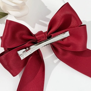 Close-up of dark red satin bow hair clip with silver metal alligator clip mechanism