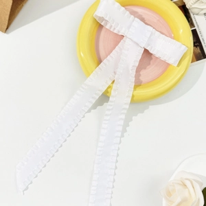 Detailed close-up of white ruffled satin bow hair clip with long flowing ribbons