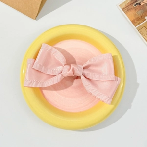 Detail of pink satin bow hair clip with double-layer ruffles on a decorative ceramic plate