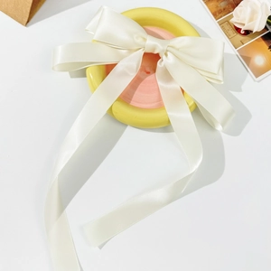 Detail of elegant cream satin ribbon bow hair clip on a minimalist decorative tray
