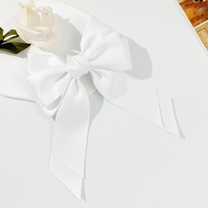 Close-up of elegant white satin bow hair clip with long ribbons on a stylist tray