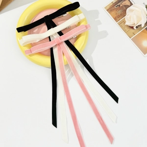 Three velvet bow hair clips in black, cream, and pink with long ribbons on a yellow tray