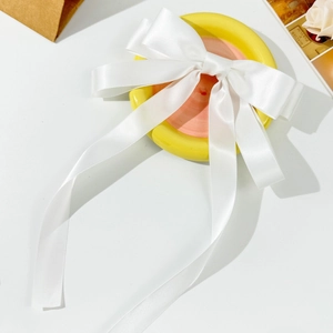 Elegant white satin bow hair clip with long ribbons on a yellow decorative plate