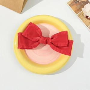 Detailed top view of a red ruffled silk bow hair clip on a decorative ceramic plate