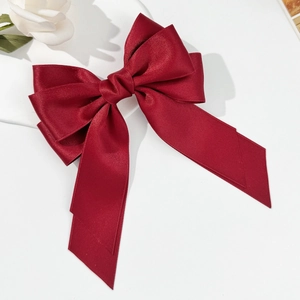 Macro view of a premium burgundy satin bow hair clip with long silk ribbons on white