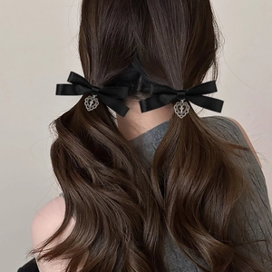 Detailed view of black ribbon bow hair clips with silver cross heart pendants on pigtails