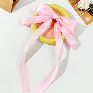 Macro shot of a large light pink satin bow hair clip with ribbons on a yellow tray