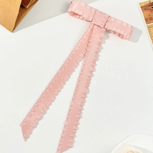 Detail of pink satin bow hair clip with ruffled edges and elegant flowing ribbon streamers