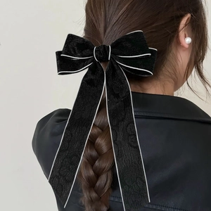 Close-up of a black velvet bow hair clip with white piping on a braided hairstyle