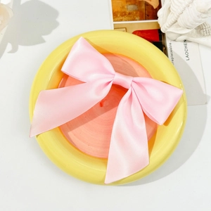 Detailed view of pink satin bow hair clip with ribbons on a stylish ceramic plate