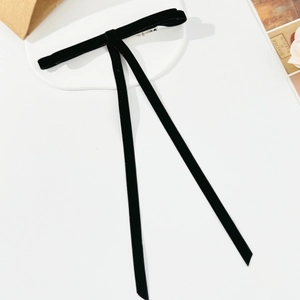 Detailed macro view of black velvet bow hair clip with long streamers on white tray