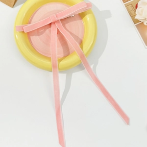 Pink velvet bow hair clip with long streamers and silver duckbill clip on a plate