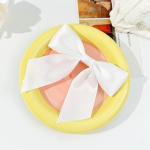 Detailed top view of a white satin bow hairclip on a colorful ceramic plate