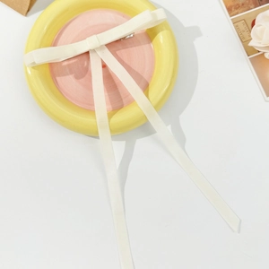 Detail of a creamy white velvet bow hair clip with long ribbons on a ceramic plate