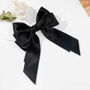 Elegant large black satin bow hair clip with long ribbons on white rose background