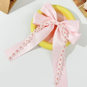 Detailed view of pink satin bow hair clip with delicate floral embroidery on long ribbons