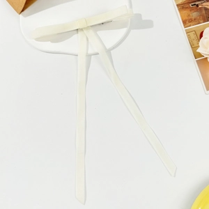 Elegant cream velvet bow hair clip with long streamers on a white decorative tray