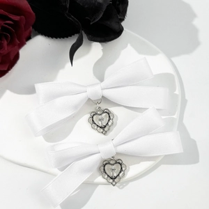 Detail view of white satin bow hair clips with silver cross heart pendants