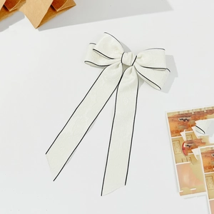 Detailed macro view of white bow hair clip with black piping and jacquard texture