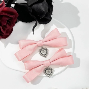 Detail of pink satin bow hair clips with silver heart cross charms on a display tray