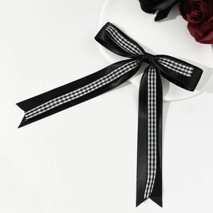 Détail du nœud papillon en satin noir avec ruban damier et longues lanières élégantes