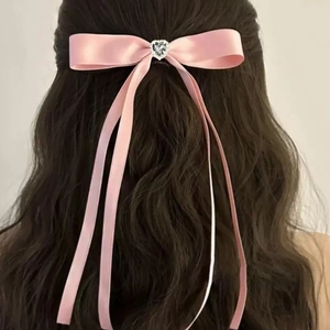 Close-up of pink satin ribbon hair clip with heart rhinestone on long wavy brown hair