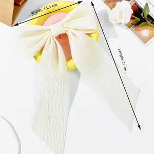 Detail view of cream oversized bow hair clip with vertical pleated texture and long ribbons