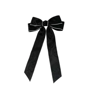 Elegant black bow hair clip with white trim and floral embossed texture on long ribbons