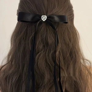 Detail of a black satin bow hair clip with heart rhinestone on long wavy hair