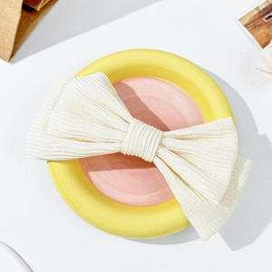 Detailed top view of a cream bow hair clip with ribbed texture on a decorative plate