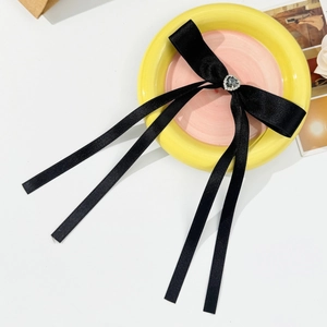 Detail of black satin bow hair clip with heart rhinestone on a yellow ceramic plate