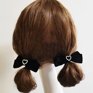 Detail of two black velvet bow hair clips with heart-shaped crystal rhinestones on a model