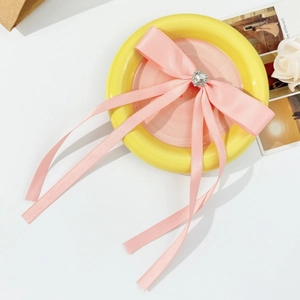 Pink ribbon bow hair clip with heart rhinestone center shown on yellow ceramic plate