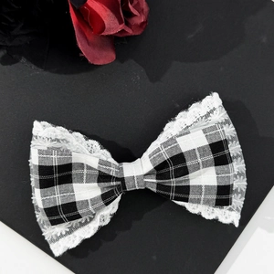 Macro detail of houndstooth bow hair clip with white lace trim on a matte black background
