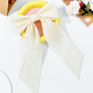 Close-up of cream bow hair clip featuring elegant vertical pleated texture and long ribbons