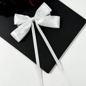 Elegant white satin bow hair clip with lace trim and long ribbons on minimalist background