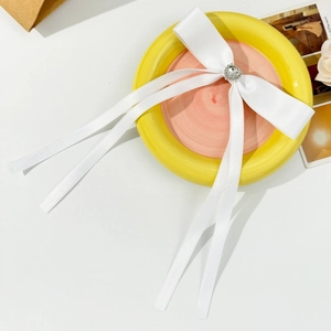 Close-up of white satin bow hair clip with heart rhinestone on a stylish ceramic plate