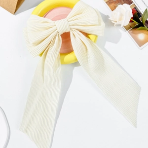 Elegant cream pleated bow hair clip with long ribbons on decorative ceramic bowl
