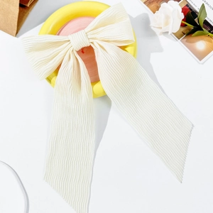 Elegant cream bow hair clip with pleated chiffon texture on decorative pastel tray