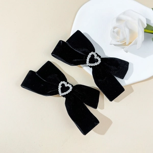 Detail of black velvet bow hair clips with silver heart rhinestone on a white plate