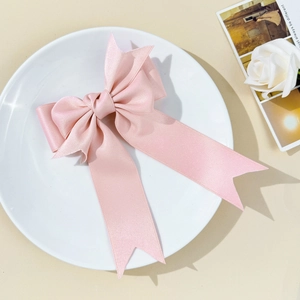 Détail de la barrette à nœud en satin rose avec de longs rubans sur une assiette blanche