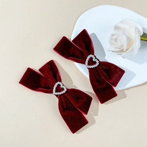 Vintage dark red velvet bow hair clips with heart rhinestone accents on a beige background