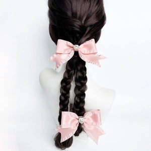 Dettaglio di fiocchi in raso rosa con strass a cuore su eleganti trecce di capelli scuri