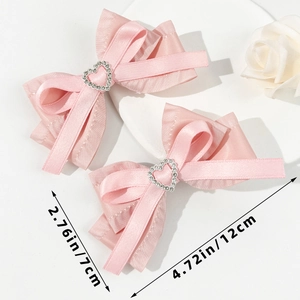 Détail des barrettes nœuds en satin rose avec strass en cœur et dimensions de 12 cm de large
