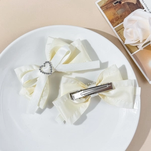 Détail de barrettes à nœuds en satin blanc cassé avec strass cœur sur plat céramique