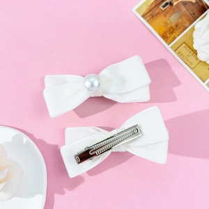 Detail showing two white velvet bow hair clips with pearl accents and metal duckbill clips