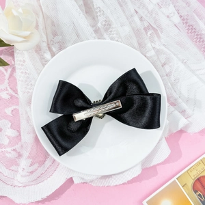 Detailed back view of a black satin bow hair clip showing the silver metal duckbill clip
